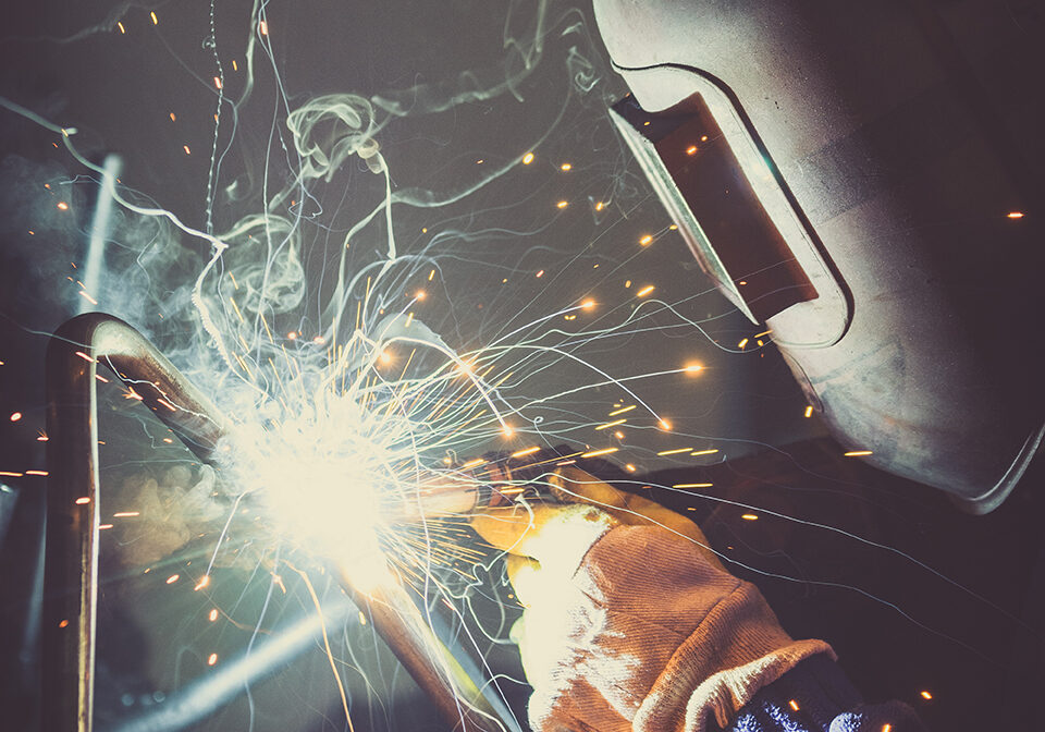 Industrial worker welding round pipe on a work table, producing